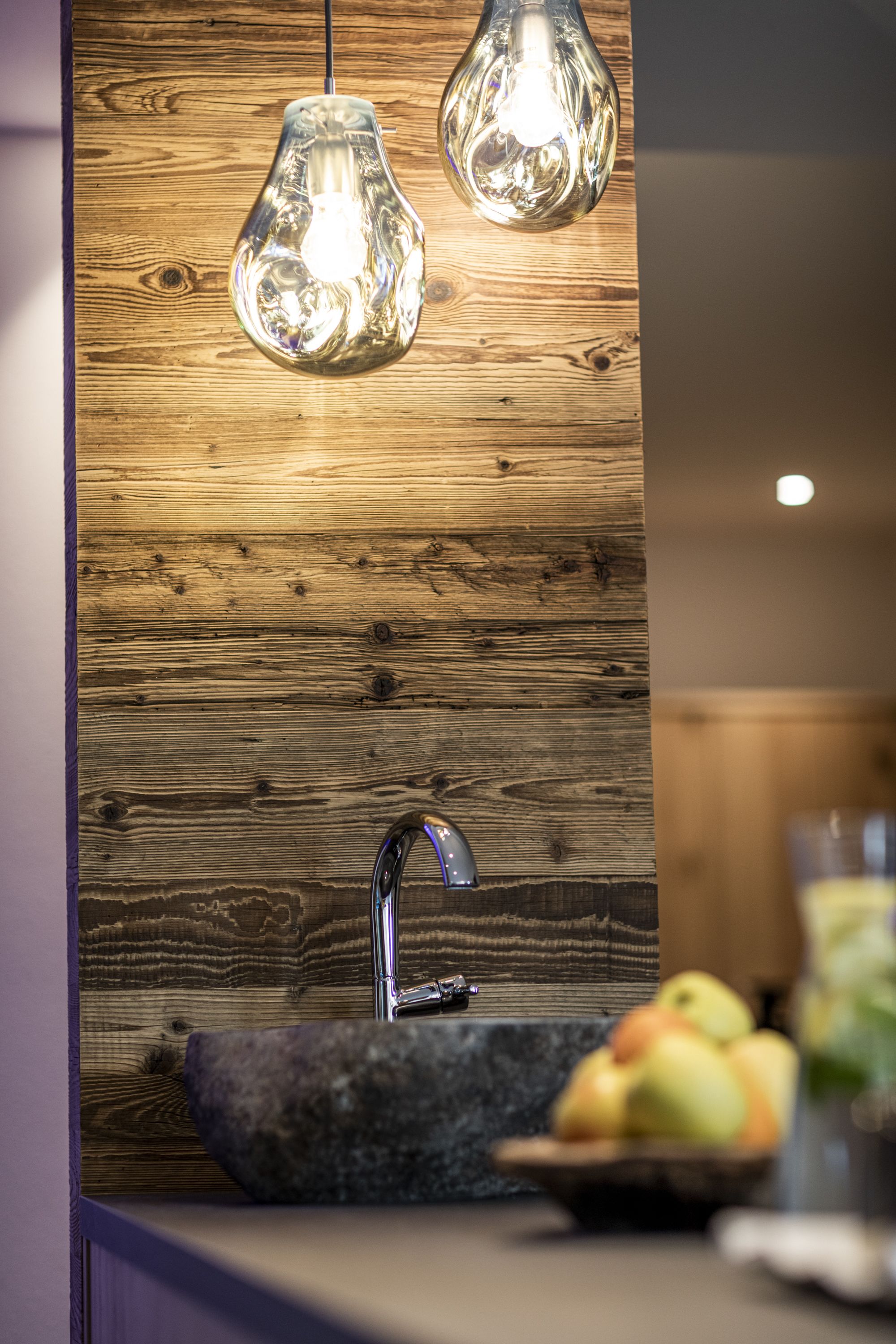 Una cocina moderna con salpicadero de madera, un lavamanos de granito e iluminación colgante.