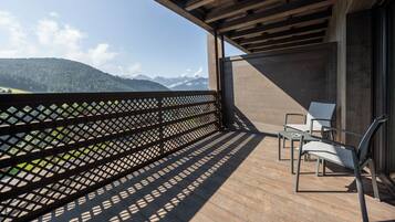 A wooden balcony with a view of mountains, two white chairs, and a table.