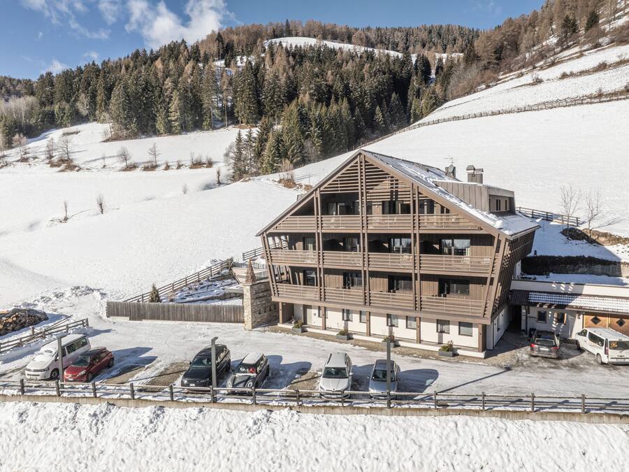 Un edificio in legno a più piani con balconi, immerso in un paesaggio innevato e affiancato da un pendio boscoso.