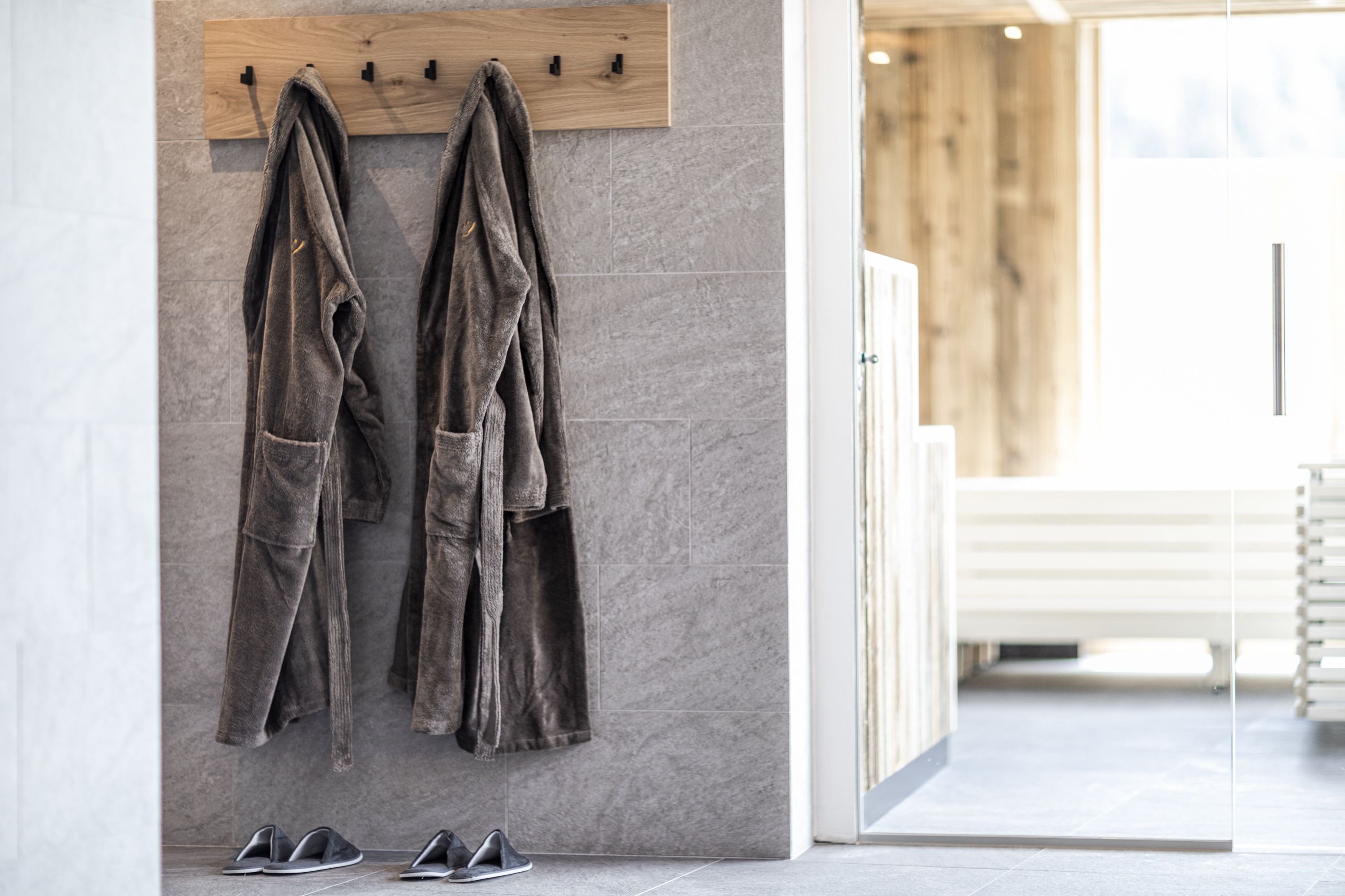 Ein Badezimmer mit einem hölzernen Handtuchhalter, der zwei Handtücher trägt, einer weißen Bank und einem Paar Schuhen auf dem Boden.