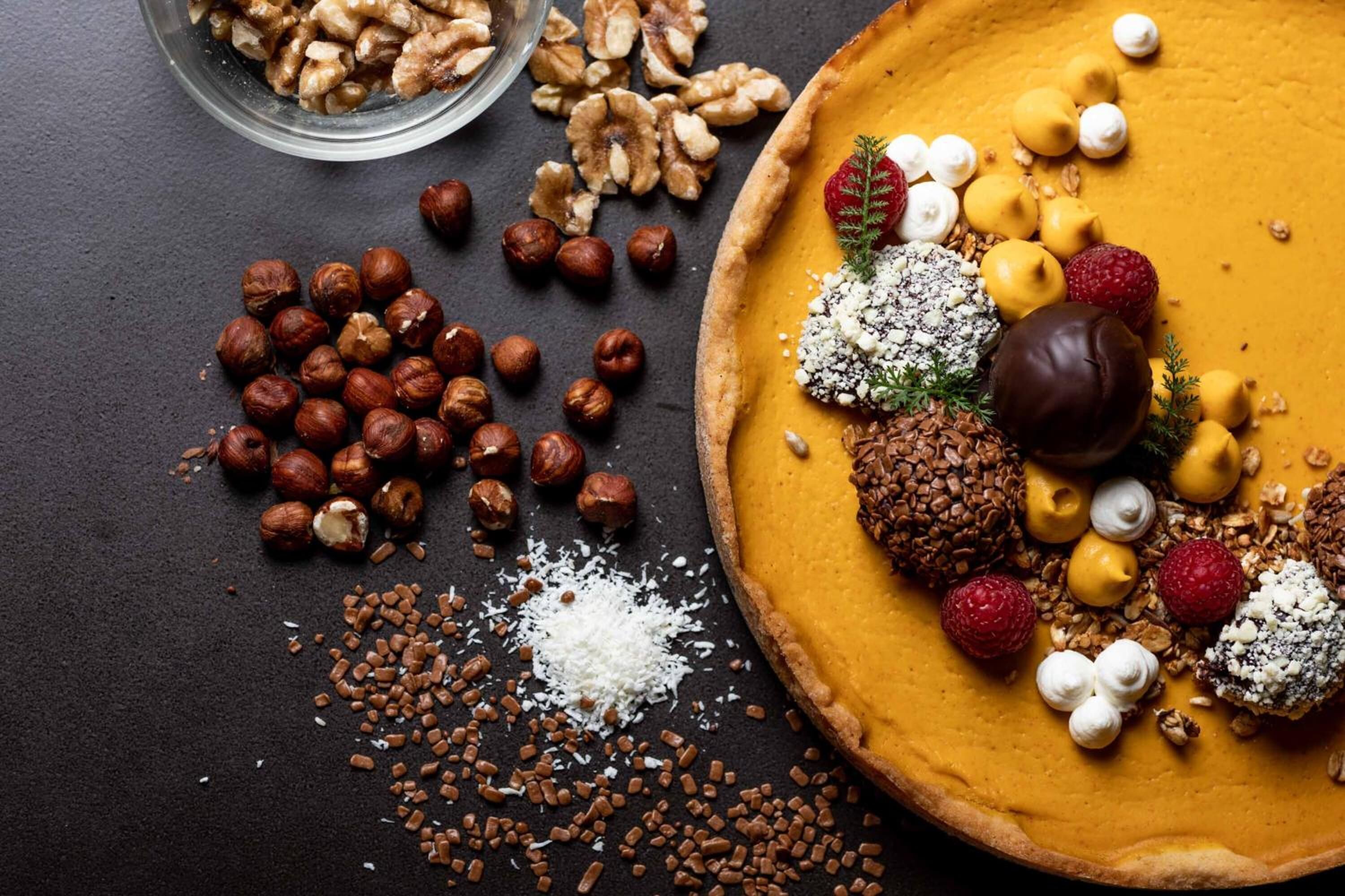 Una tarta de calabaza con diferentes ingredientes y nueces sobre una superficie oscura.