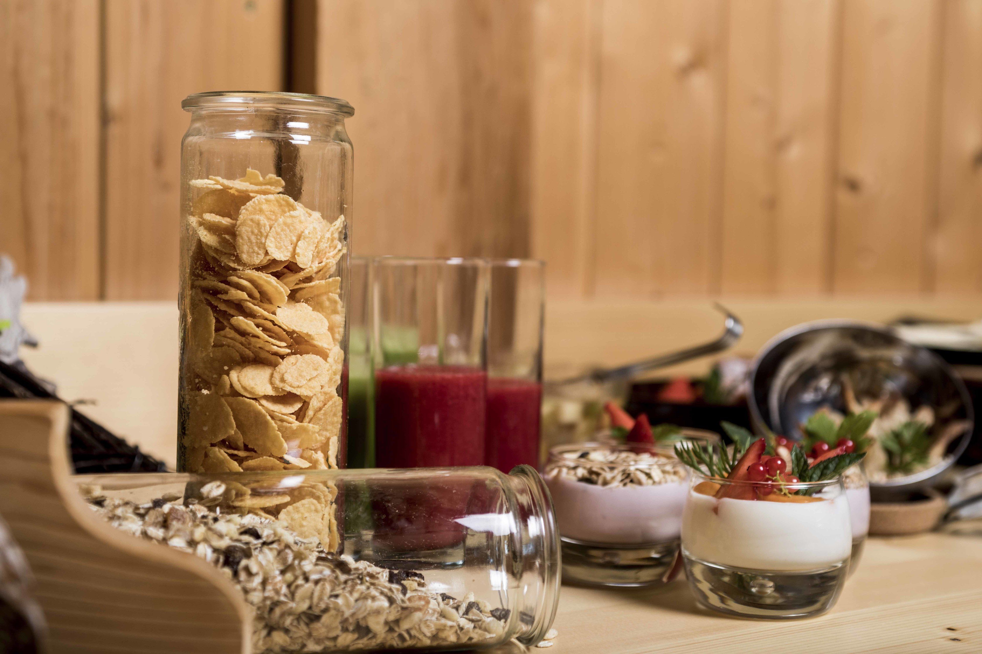 A wooden table with various food items, including a jar of cereal, a glass of smoothie, and small bowls of yogurt with fruits.