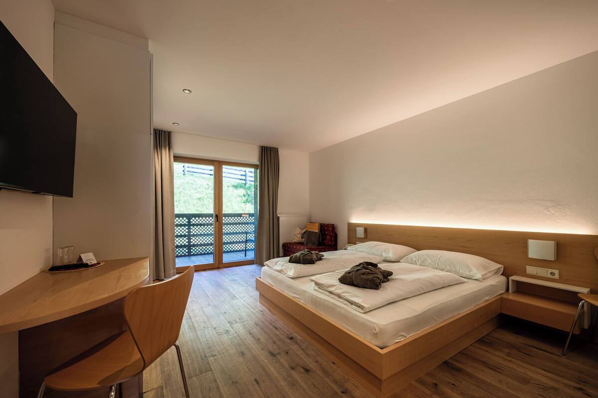 A modern hotel room with a large bed, a desk, and a TV.