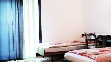 A room with two single beds, a wooden floor, a window with curtains, and a chair.