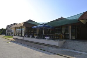 A building with a covered outdoor seating area, a clear sky, and a paved walkway. - Motel Licki Krovovi (Gracac)