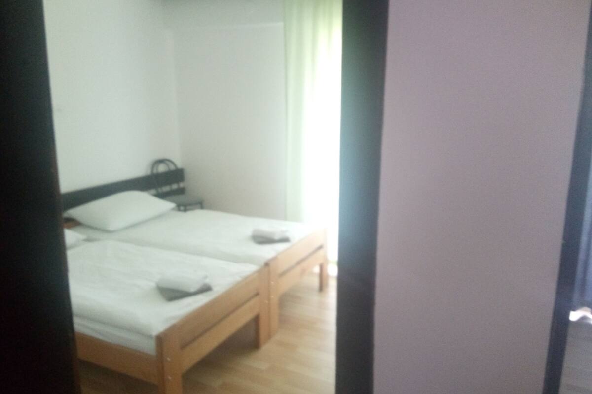 Ein Doppelbett mit Holzrahmen und weißer Bettwäsche, ein Nachttisch und ein Fenster mit Vorhang.