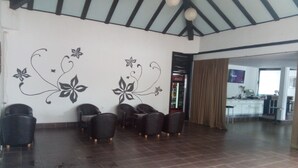 Una habitación amplia con techo alto y suelo de baldosas, que incluye una zona de estar con varias sillas y una pared decorada con motivos florales.