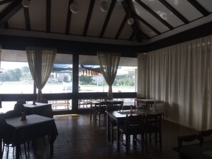 A restaurant with a high ceiling, wooden beams, and large windows with curtains. Tables and chairs are arranged for dining. - Motel Licki Krovovi (Gracac)