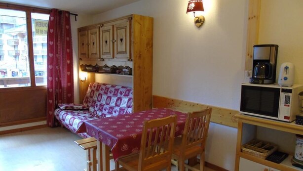 A compact room with a wooden table and chairs, a sofa, a small kitchenette with a microwave, and a window with curtains.