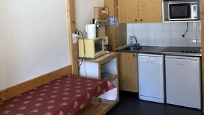 A compact kitchenette with wooden cabinets, a microwave, a toaster, and a washing machine.