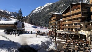 A ski resort with a wooden building with balconies, a ski lift, and a mountain backdrop.