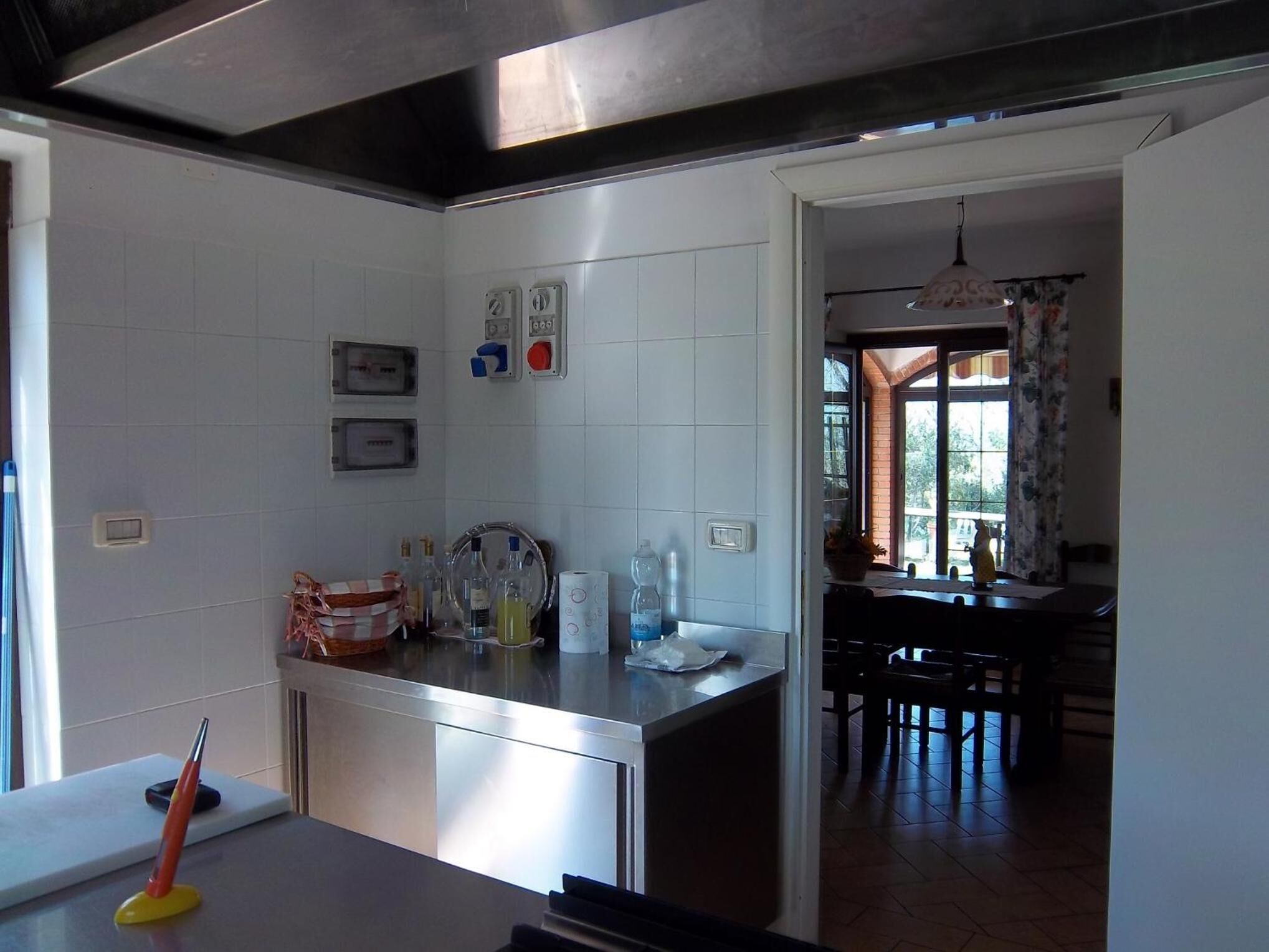 A modern kitchen with white tiles, a stainless steel countertop, and a dining area with a table and chairs.