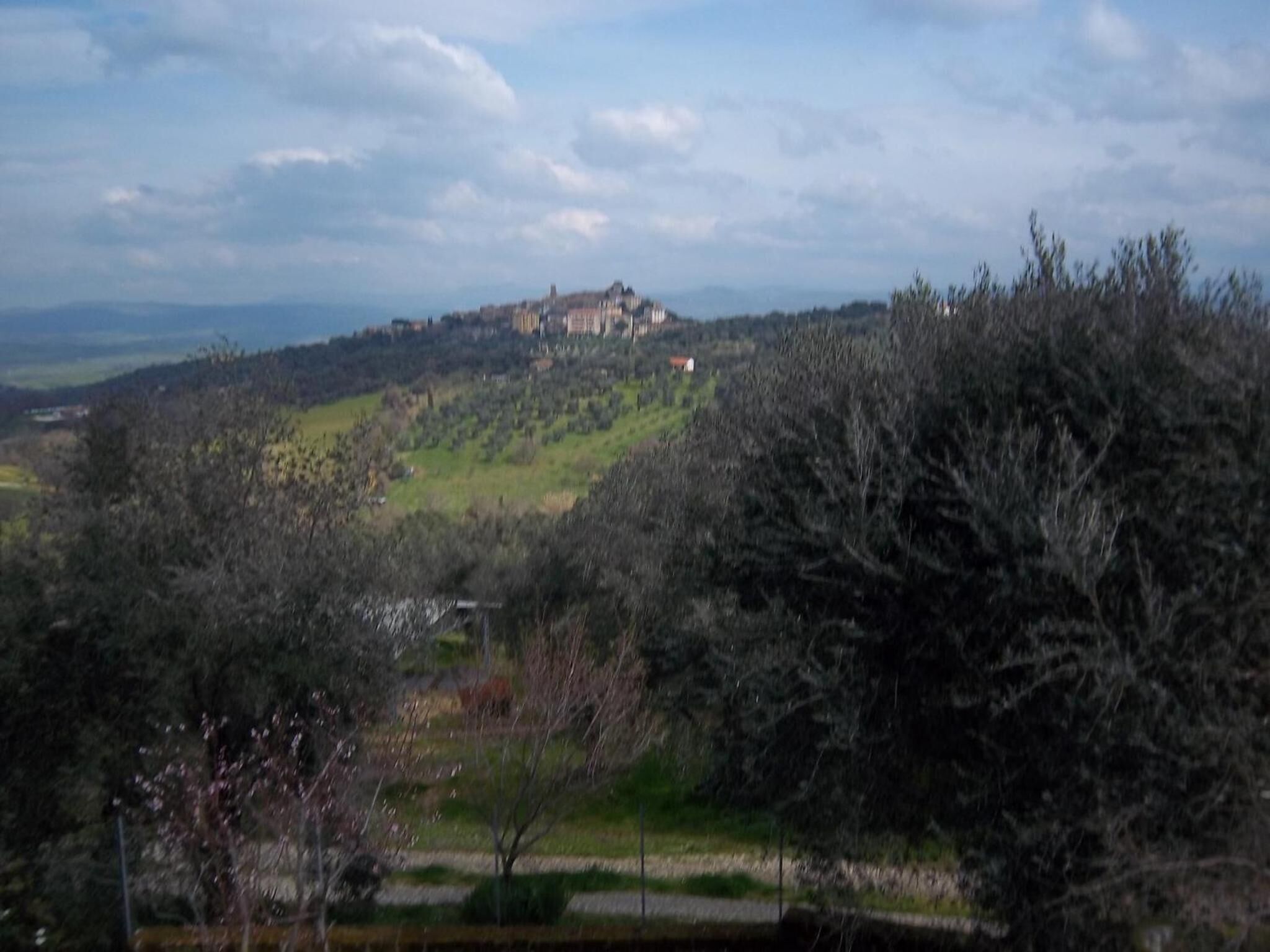 Une vue d’un sommet de colline avec un bâtiment, entouré d’arbres et de champs ouverts.