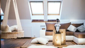 A cozy living room with a macrame hanging chair, a wooden coffee table, and a sofa with cushions. There are two windows providing natural light. - Golden Angel Apartment (Prague)