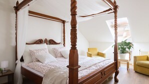 A four-poster bed with a canopy, a yellow armchair, and a potted plant in a room with wooden flooring and a sloped ceiling. - Golden Angel Apartment (Prague)