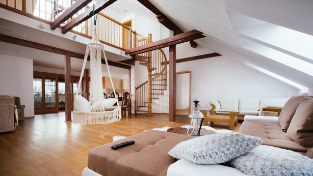 A spacious loft-style living area with a high ceiling, wooden beams, a staircase, and a cozy seating area with a sofa and ottoman. - Golden Angel Apartment (Prague)