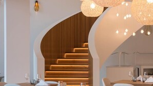 Un área de comedor moderna con mesas redondas, sillas blancas y una escalera con escalones de madera.