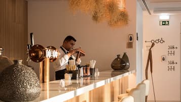 A modern bar area with a bartender, wooden paneling, and hanging light fixtures.
