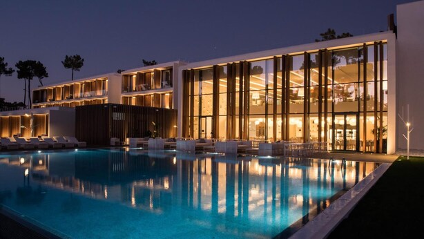 Un hotel moderno con piscina, varios balcones e interiores bien iluminados.