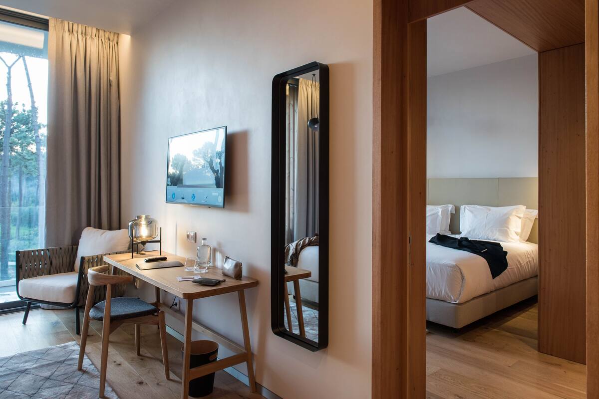 Ein Hotelzimmer mit Bett, Schreibtisch mit Stuhl, großem Spiegel und einem Fenster mit Vorhängen.