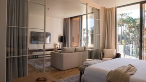 Habitación de hotel moderna con una cama grande, un sofá, una silla, un televisor y una puerta corredera de vidrio al exterior.