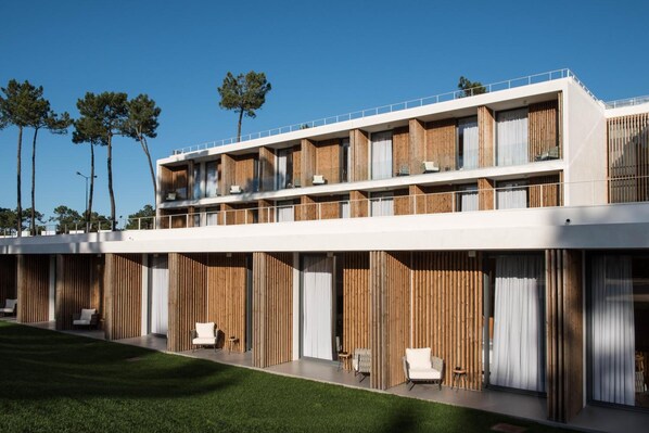 Un hotel moderno con techo plano, varios balcones y un césped bien cuidado.