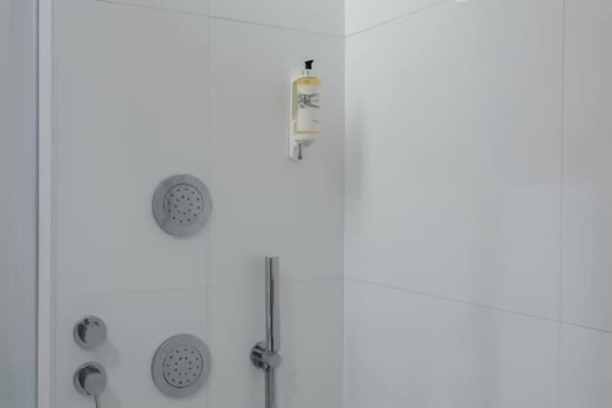 A modern shower with multiple heads and a soap dispenser.