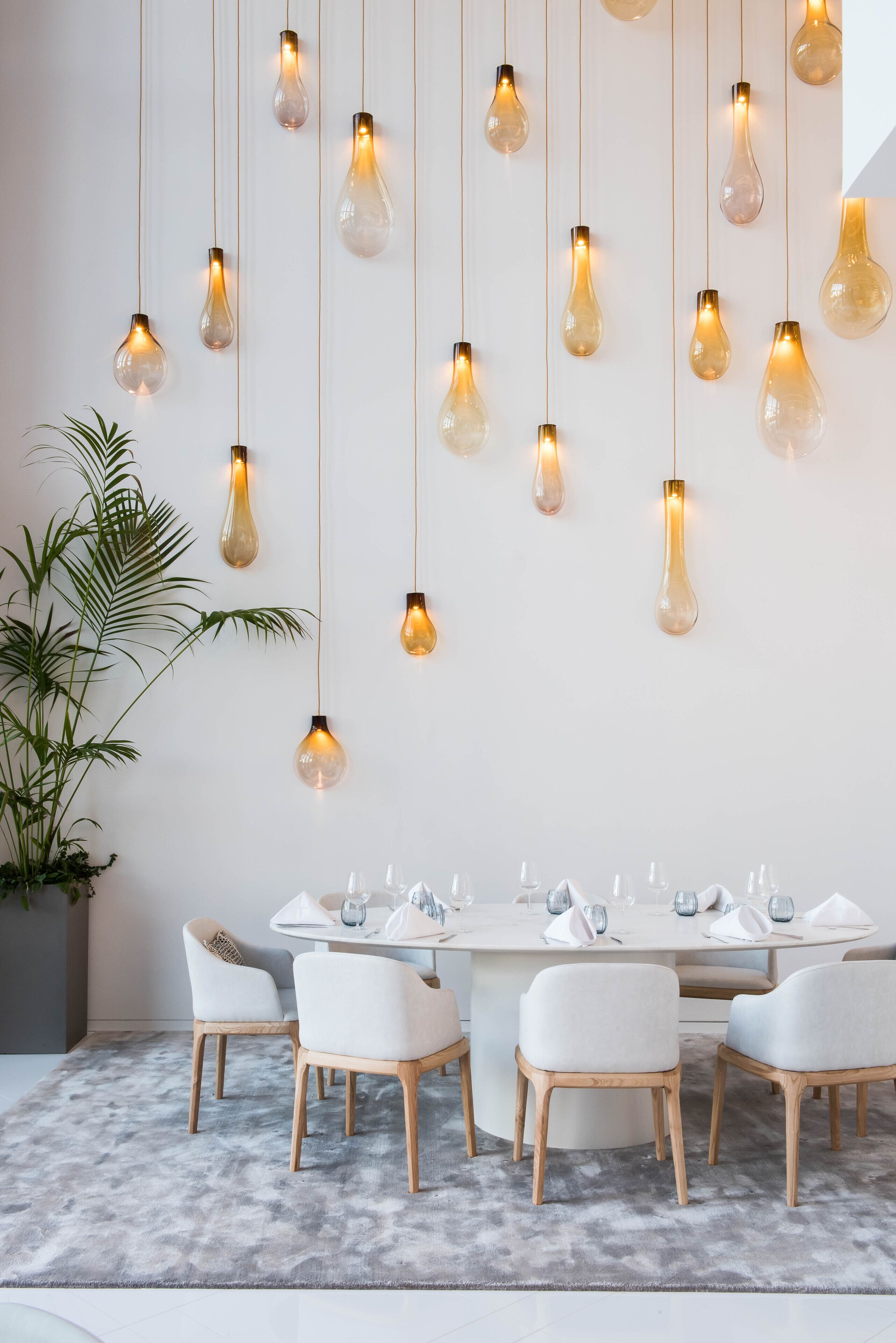 Un área de comedor moderna con una mesa redonda, sillas blancas y lámparas colgantes.