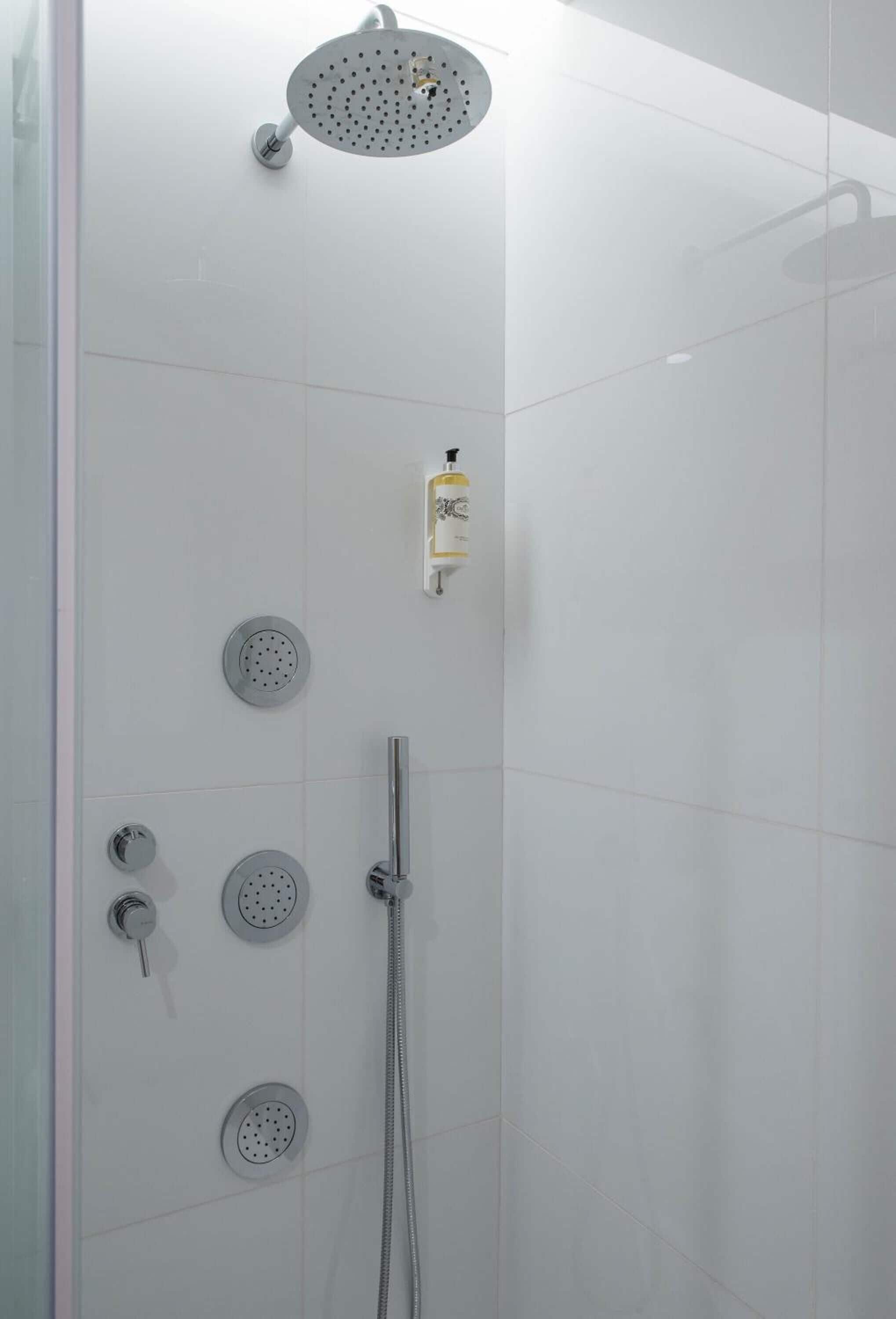A modern shower with multiple heads and a control panel.