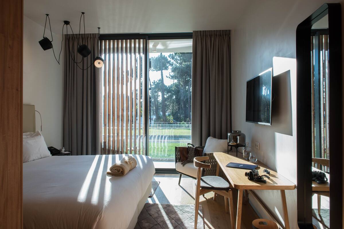 Ein Hotelzimmer mit Bett, Schreibtisch, Sessel, Fernseher und Blick ins Freie.