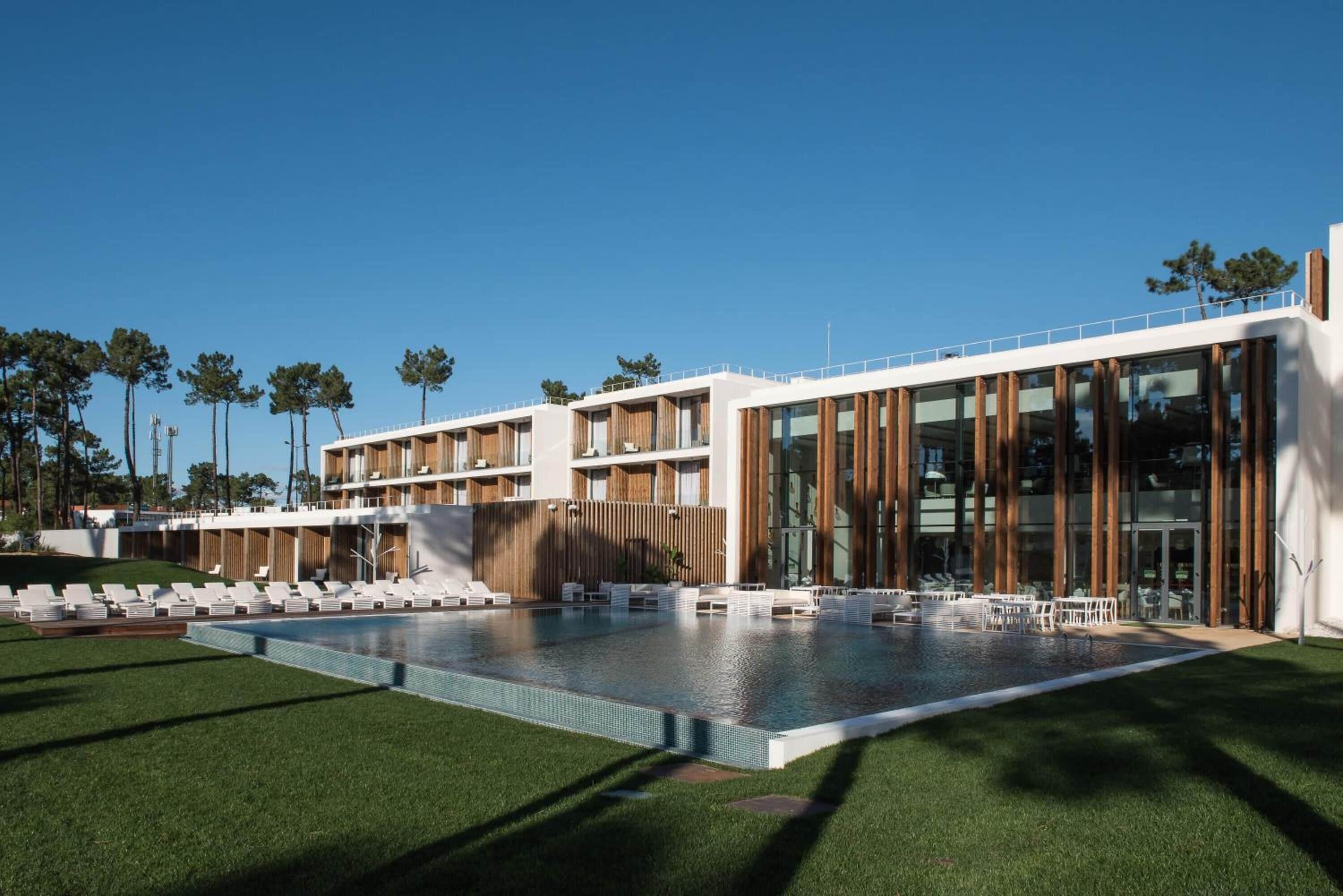 Un hotel moderno con una piscina grande, zona de estar exterior y vistas claras del paisaje circundante.
