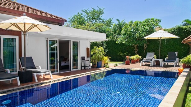 Ein Pool mit Liegestühlen und Sonnenschirmen, umgeben von einem Garten und einem Gebäude mit Ziegeldach.