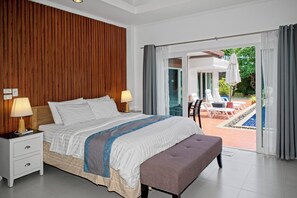 A hotel room with a bed, bedside tables, a bench, and a view of an outdoor pool area.