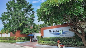 Schild für Busaba Pool Villas mit freiem Blick auf den Eingang, einen von Bäumen gesäumten Weg und einen abgestellten Roller.