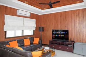 A living room with a leather sofa, a glass coffee table, a flat-screen TV, and a ceiling fan. - Busaba Villa 11 - 4 Bedroom - Pool (Hua Hin)