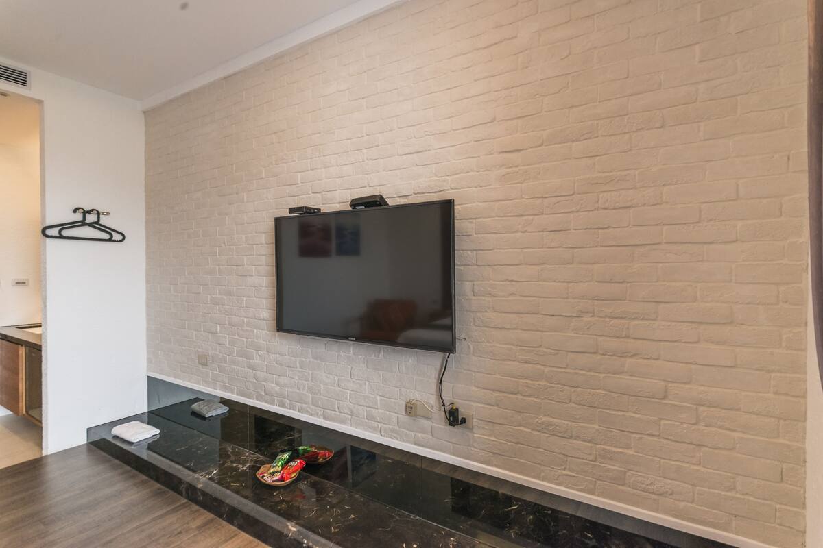 A modern living room with a flat-screen TV mounted on a brick wall, a black marble countertop, and a small shelf with a towel and snacks.