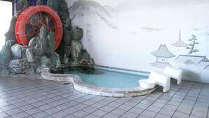 Une piscine avec une roue à eau rouge, des rochers et un mur décoré de mosaïques.