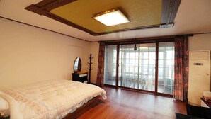 Une chambre avec un grand lit, une table de chevet, un miroir, un porte-manteau et une porte-fenêtre coulissante donnant sur un balcon.
