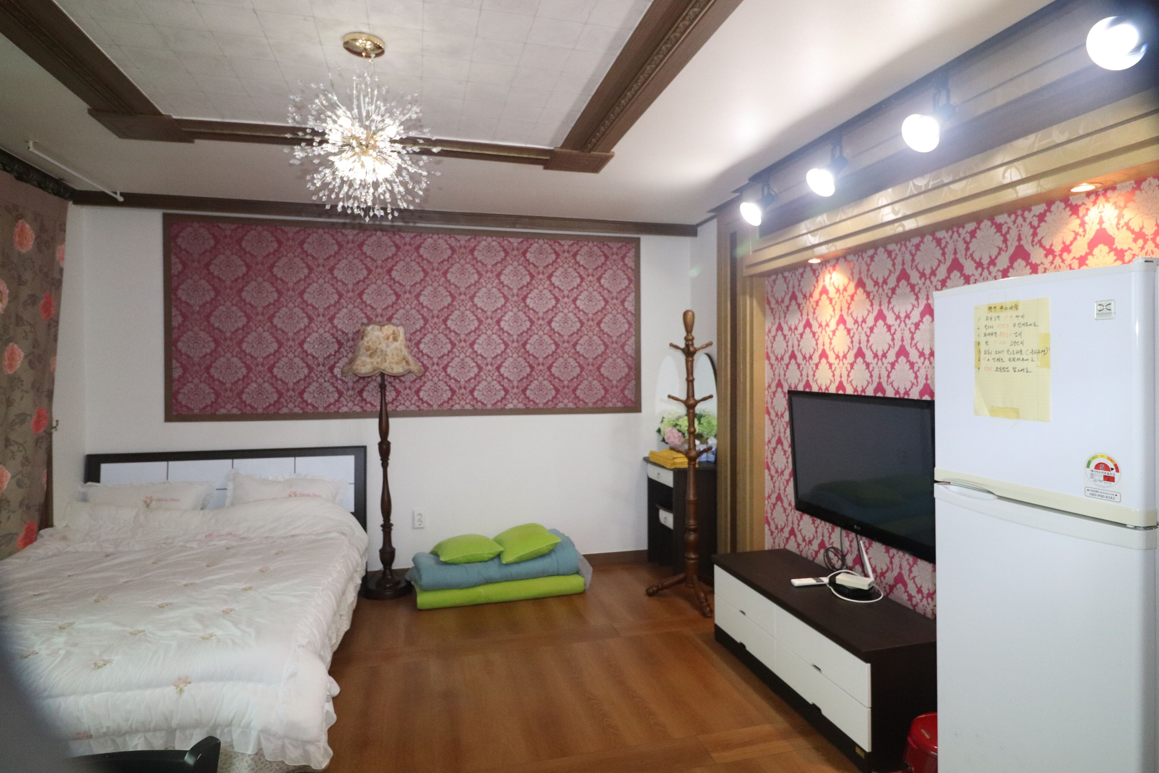 Un dormitorio con cama, televisión, refrigerador y una lámpara decorativa.