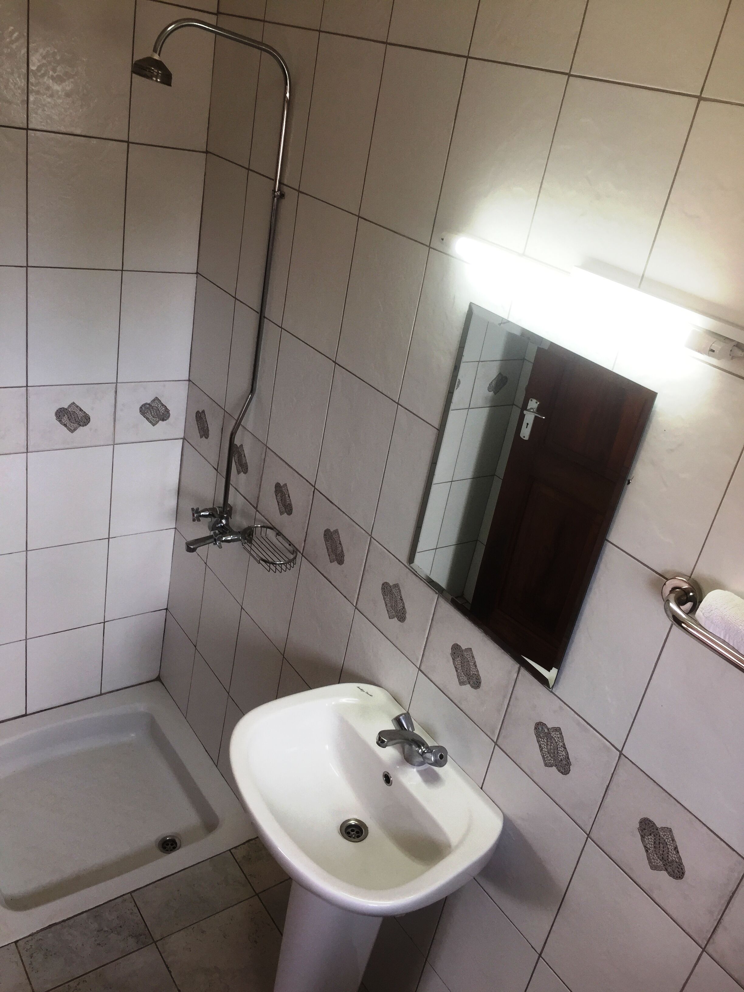 Un baño con lavamanos blanco, ducha y espejo.