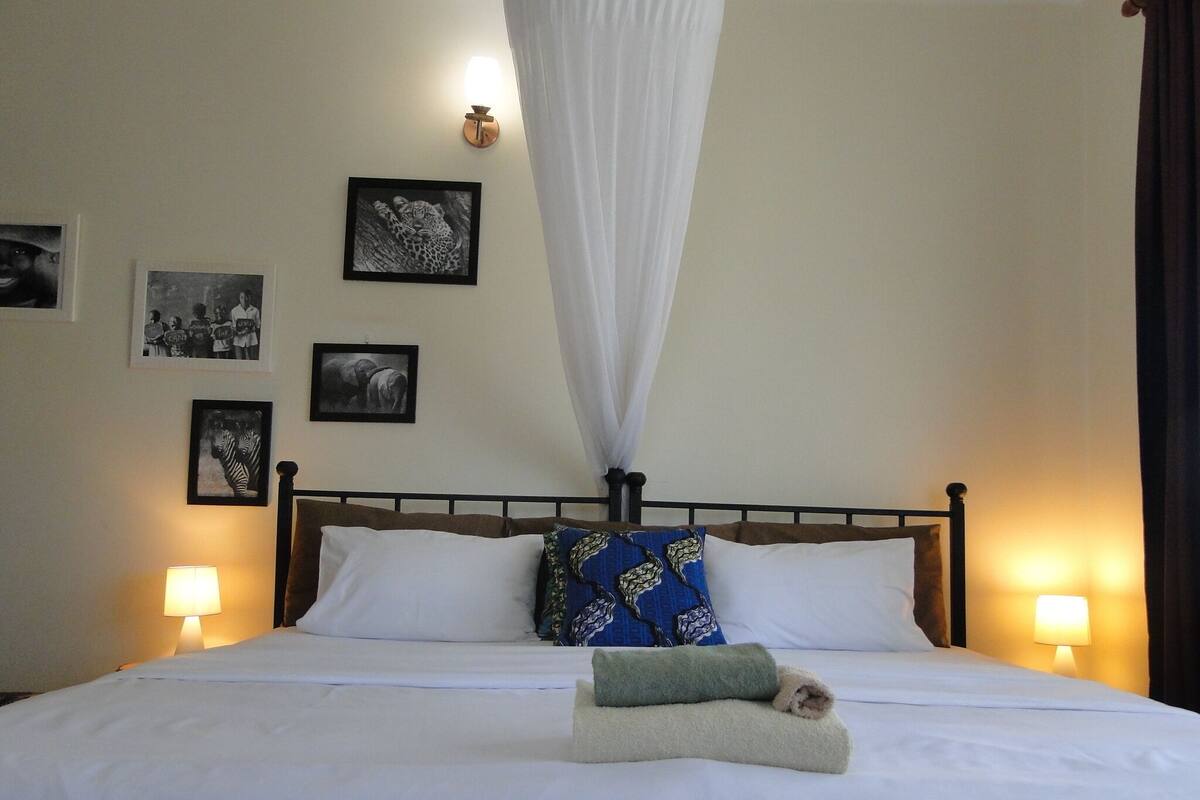 A neatly made bed with white linens, a canopy, and two bedside lamps.
