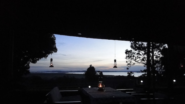 An outdoor seating area with tables and chairs, overlooking a body of water with distant land and trees.