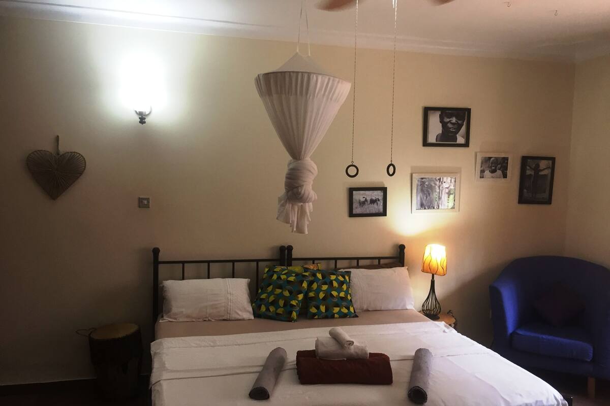 A bedroom with a bed, a hanging mosquito net, a lamp, and a blue chair.