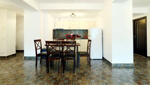 A modern kitchen with white cabinets, a dining table with chairs, and a tiled floor. - Apartment Sofia (Sinaia)