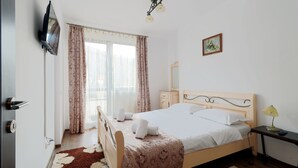 A bedroom with a bed, a bedside table, a lamp, a TV mounted on the wall, and a window with curtains. - Apartment Sofia (Sinaia)