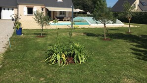 Une maison d’habitation dotée d’une piscine, d’un patio couvert et d’une pelouse bien entretenue agrémentée de petits arbres.