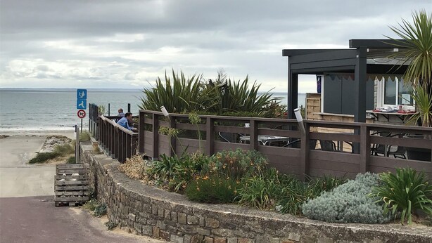 Une promenade en bord de mer, agrémentée d’une clôture en bois, d’un mur de pierre et offrant une vue sur la mer.