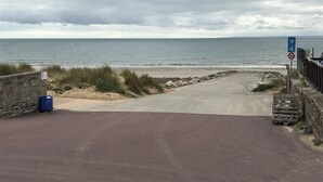 Une route côtière menant à la plage, avec un panneau indiquant que les chiens ne sont pas autorisés.