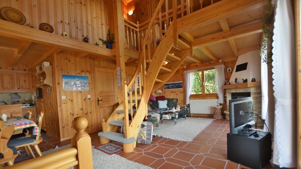A wooden cabin interior with a staircase, a dining area, a kitchen, and a fireplace. - Chalet Joshua (Heremence)