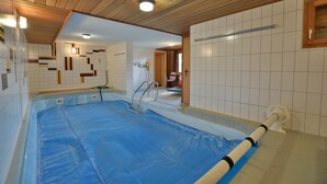 A swimming pool with a blue cover, wooden ceiling, and white tiled walls. - Chalet Joshua (Heremence)